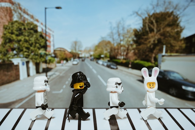 Изображена сцена, вдохновленная знаменитой обложкой альбома The Beatles Abbey Road, 
                  но с использованием фигурок LEGO. Четыре фигурки штурмовики и дарт вейдер LEGO пересекают пешеходный переход, 
                  имитируя позу участников группы Beatles на оригинальной обложке. 
                  За фигурами виден фон с улицей, похожей на улицы Лондона, с характерными домами и машинами